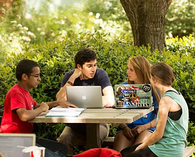 photo: four students at picnic table, conferring with laptops, notes